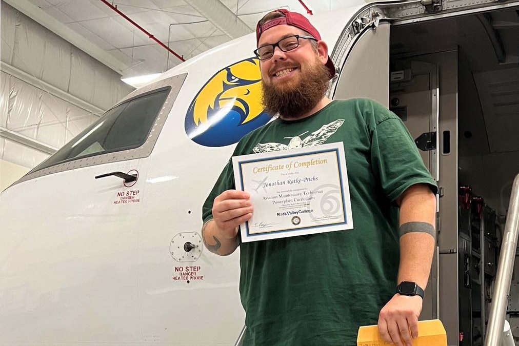Smiling man holding a certificate and standing on the stairs to an airplane. Photo introduces Jonothan's Success Story with The Workforce Connection.