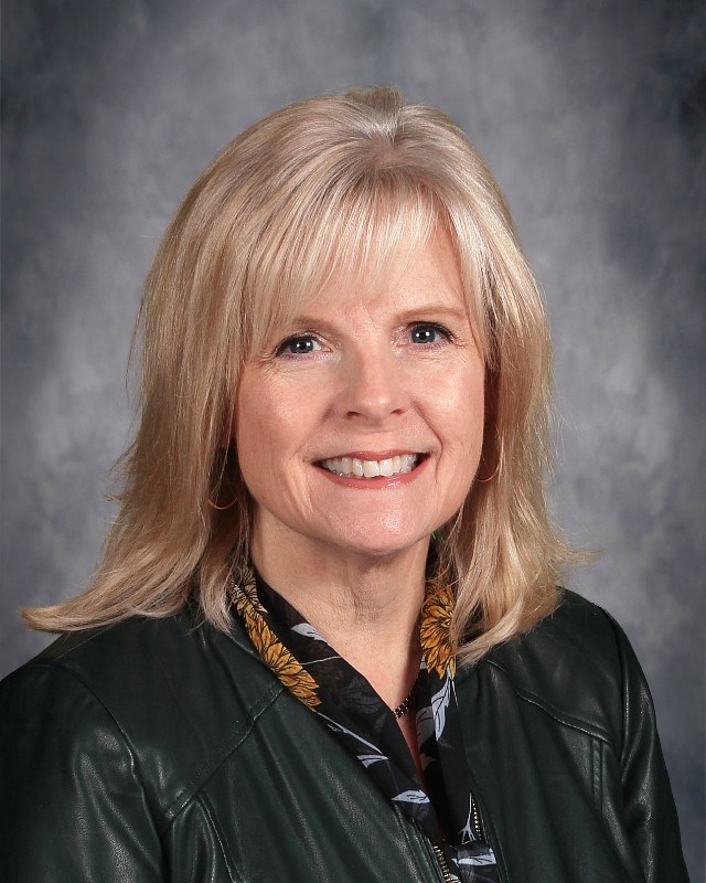 Board Member headshot photo of smiling blonde haired woman wearing a dark jacket.