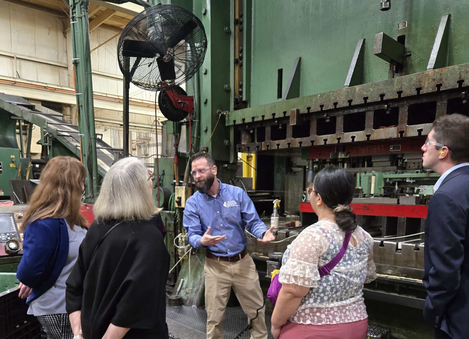 A group of people standing in front of a large machine on a tour of Rockford Toolcraft.