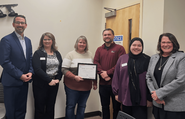 Photo of 6 people standing in a row with one holding a framed certificate for a Business Leadership Award.