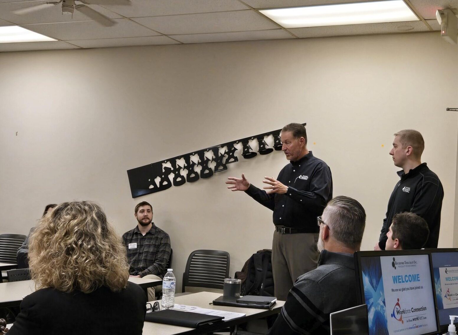 2 men in black shirts giving a talk during a meeting.